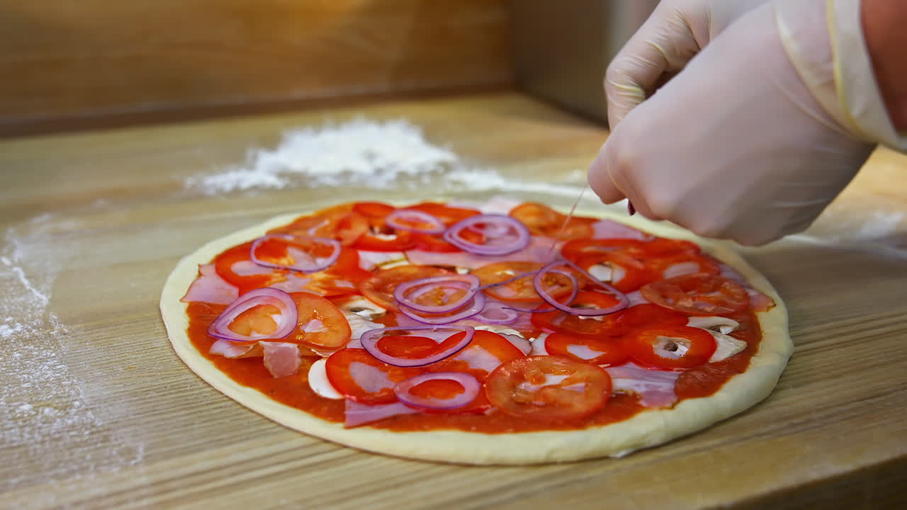 Pizza preparation.Hands putting slices of onions on pizza dough on table. Process of making pizza. Chef prepares filling for delicious pizza.