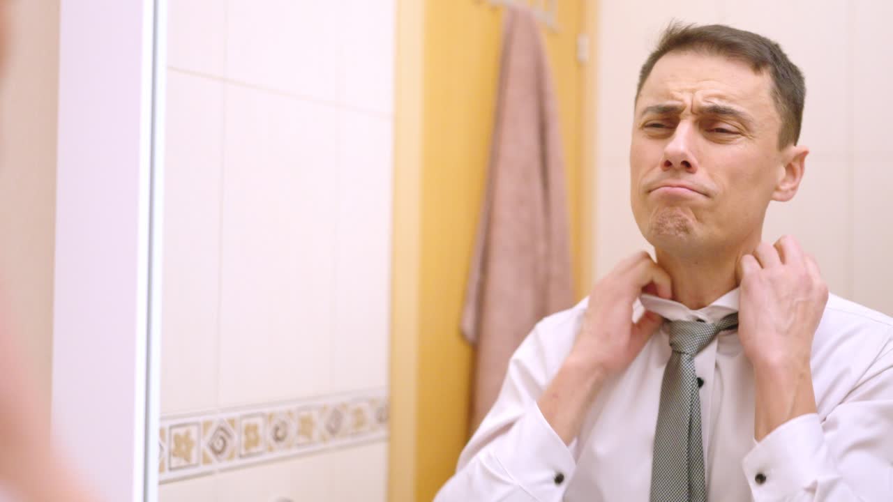 Businessman getting ready in bathroom mirror, adjusting his tie