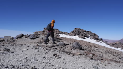 Hiker-walks-on-remote-rocky-mountain-summit-trail-on-cold-blue-sky-day