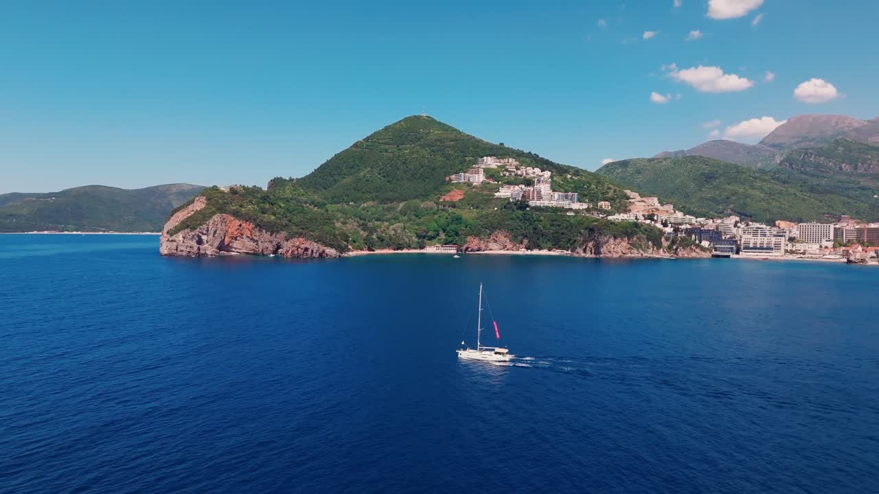 Svago di lusso: foto aerea di una barca a vela in una baia con villaggio costiero sullo sfondo