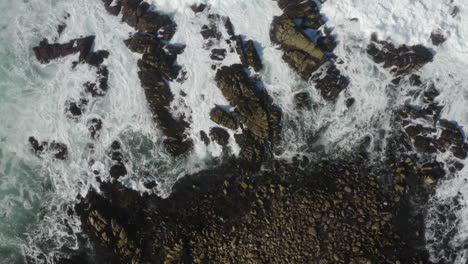 4K-overhead-corkscrew-of-stormy-seas-breaking-on-rocks-as-a-seagull-crosses-the-frame