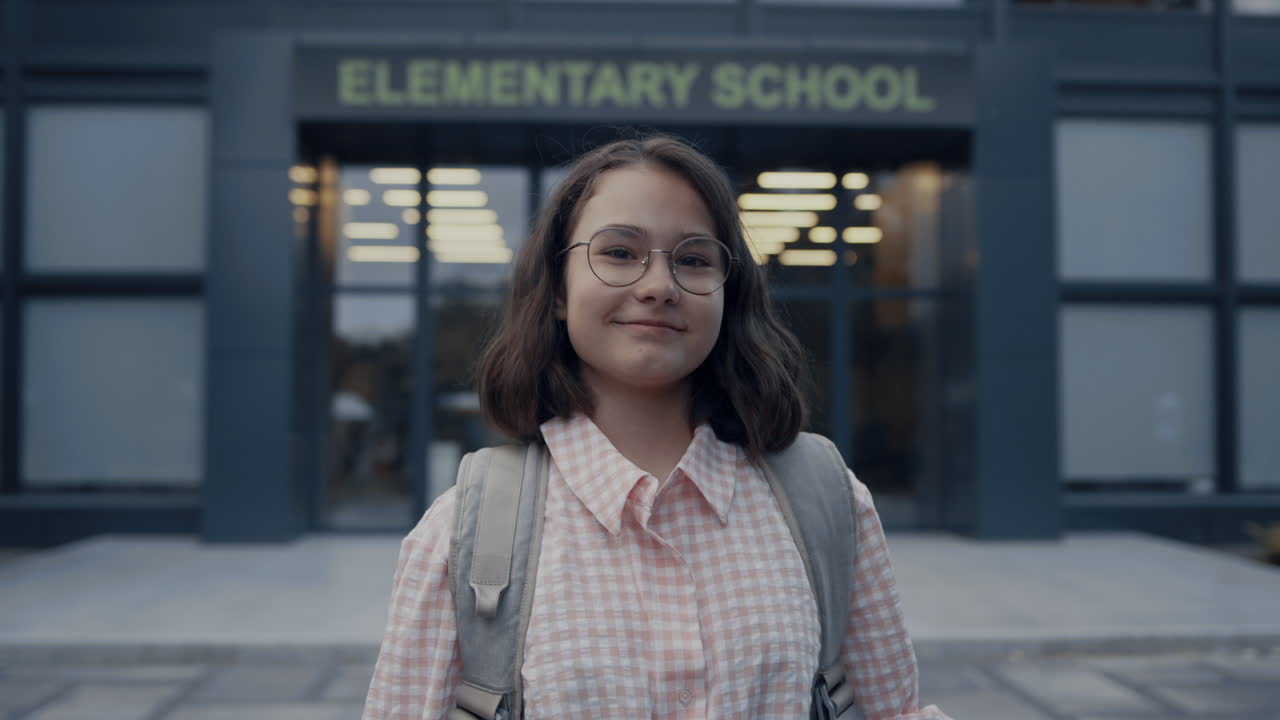 Retrato de menina sorrindo parada na entrada da escola. Adolescente olhando para a câmera.