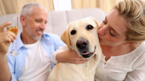 una pareja feliz acariciando a un labrador y bebiendo vino.