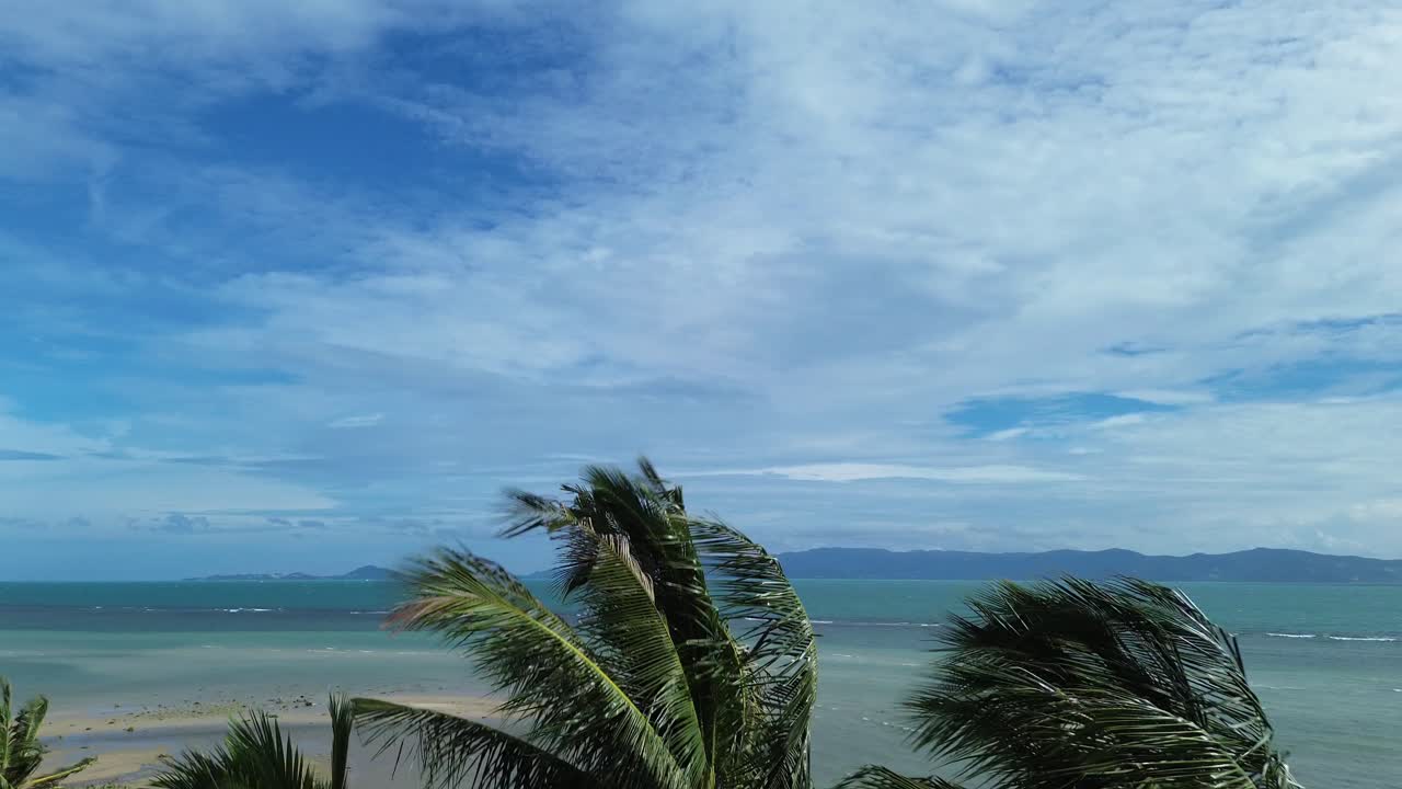 Drone footage capturing hammocks strung between palm trees on a sandy beach in Koh Phangan Thailand with turquoise sea, tropical coastline, and tranquil summer atmosphere