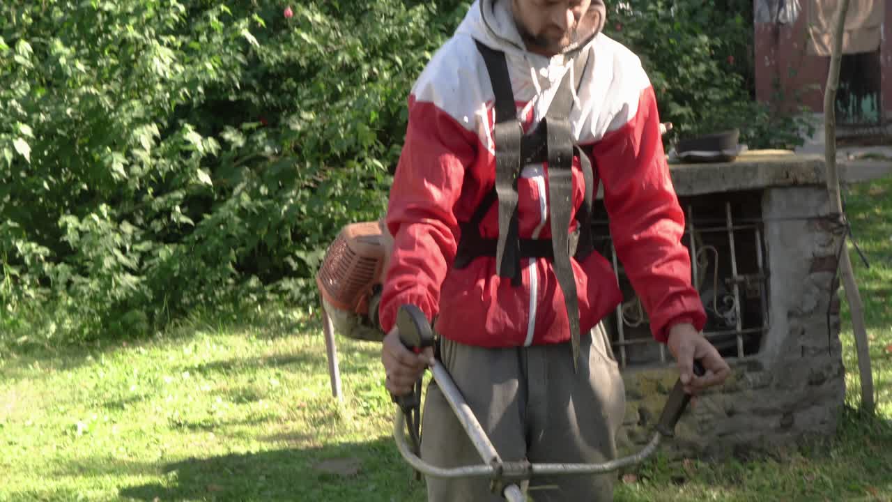 Güneşli bir arka bahçede, çim kenarlarını düzeltmek için kenar düzeltici kullanan bir bahçıvan