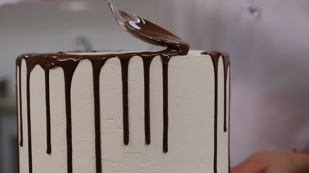 Primo piano di un pasticcere che versa cioccolato liquido da un cucchiaio su una torta.