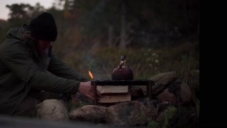 a man boiling hot water over firewoods in forest campsite