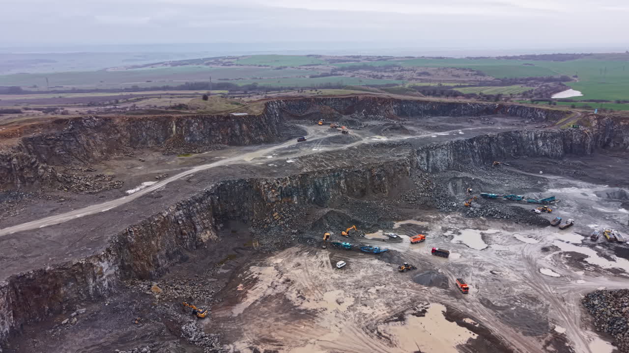 Granite quarry shows heavy machinery working in a large excavation area under cloudy sky