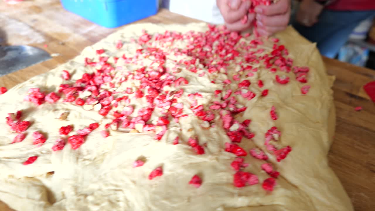 Primo piano delle mani di un fornaio che spalmano pralina rosa sull'impasto crudo.