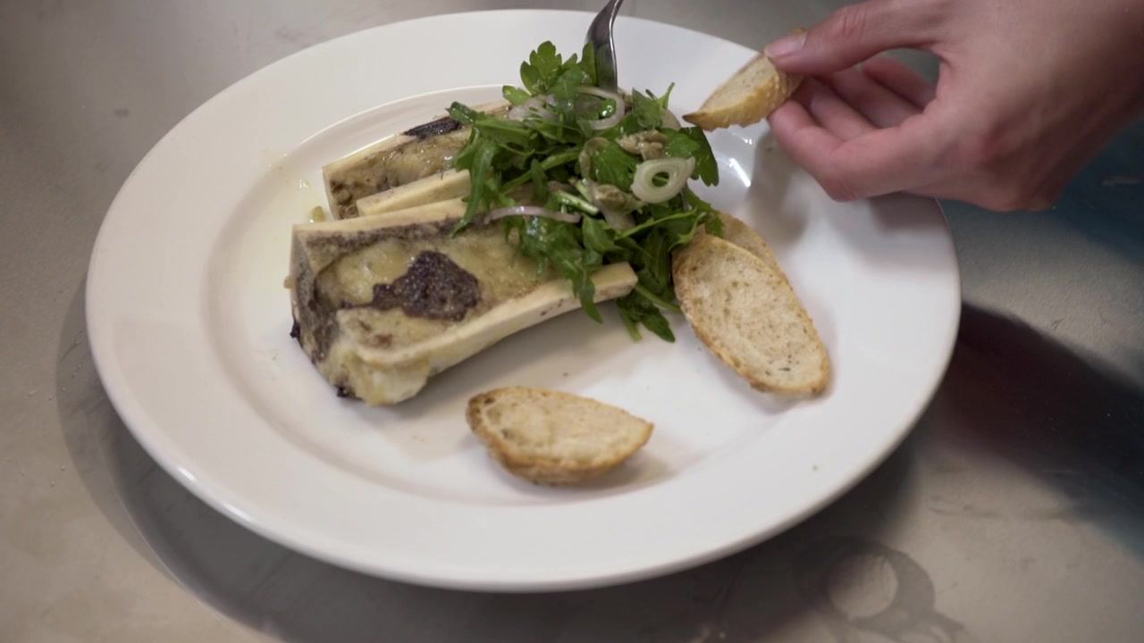 Midollo osseo con insalata di prezzemolo spalmato su toast con un cucchiaio durante una degustazione del menu per il personale di un ristorante