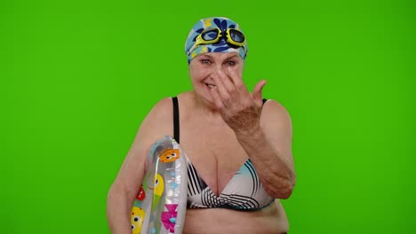 Senior-woman-tourist-in-swimsuit-bra,-swim-goggles-with-swimming-ring-asking-to-follow,-join