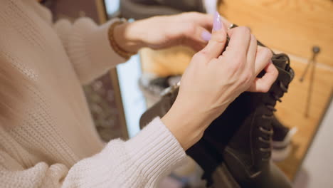 female purchaser with polished lavender manicure unzips chunky leather work boot, exploring lining for quality and comfort under warm store lighting during careful inspection before purchase