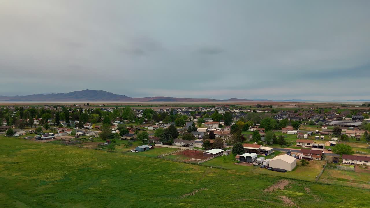 Lentävä drone kauniin vihreän ruohon yllä maalaismaisemissa ja asuinalueella Syracusessa, Utahissa, pilvisenä ja sateisena kevätpäivänä