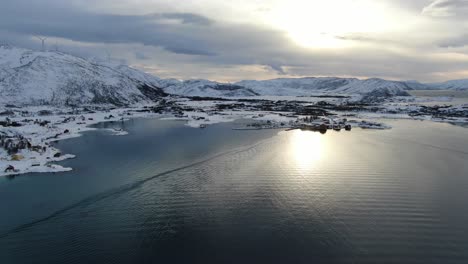 drone view in tromso area in winter flying over a snowy islands surrounded by the sea in and wind mills on the mountain in norway