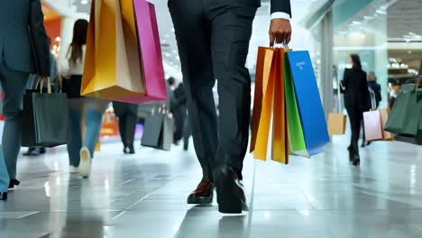 a man in a suit walks through a crowded mall with shopping bags in hand