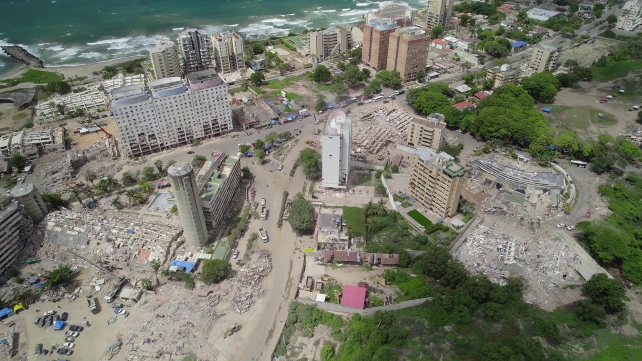 Drohnenaufnahme von schwerer Infrastrukturzerstörung in der Küstenstadt La Guaira. Mehrere Betongebäude sind zu Schutt- und Trümmerhaufen eingestürzt, Rettungsteams, Maschinen und Fahrzeuge sind im Einsatz