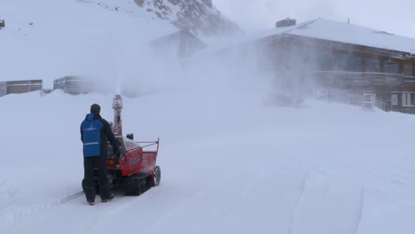 一位人在高山中晴天用吹雪机清理一条路径到房子