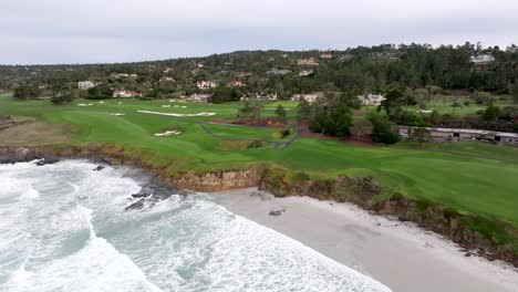 waves breaking on beach next to famous pebble beach golf course in monterey, aerial push forward shot