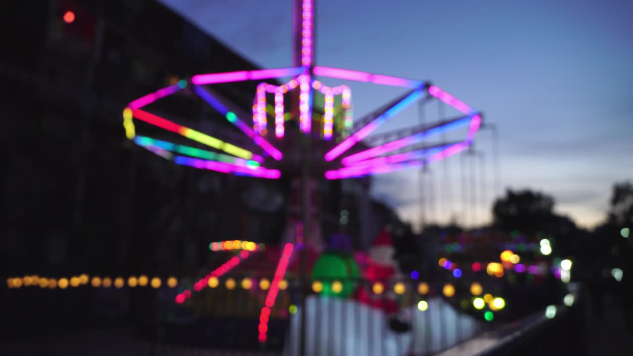 A defocused retro-illuminated carousel rotating in an amusement park.