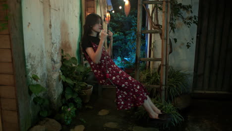 young-woman-smiles-while-sitting-on-a-swing-outside-at-night