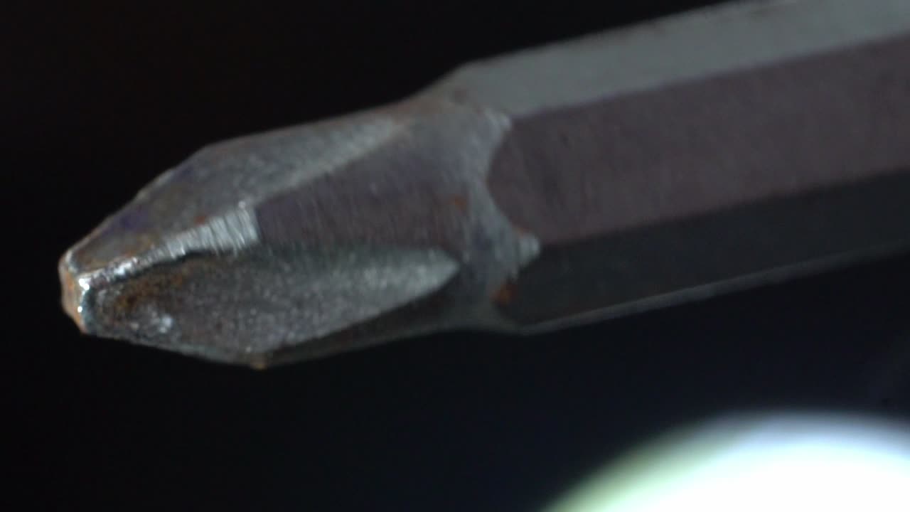 Close-up of a metal Phillips head screwdriver bit on a dark background