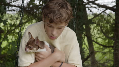 boy holding a chihuahua on a swing