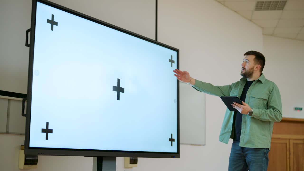 Man presenting in a spacious classroom using a large screen with a whitescreen and tracking points, ichroma key ready
