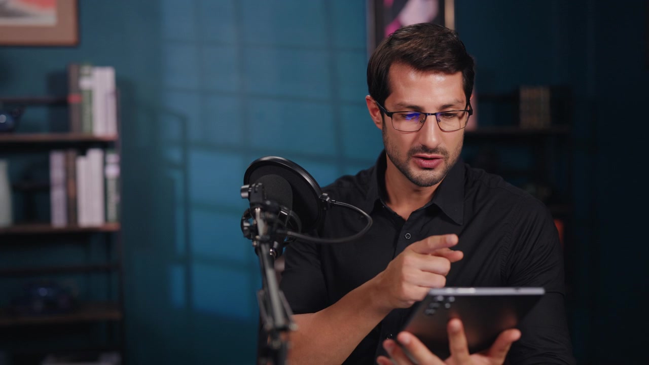 Uomo che parla al microfono mentre usa un tablet in studio