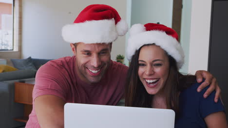 Hispanisches-Paar-Mit-Weihnachtsmützen-Und-Laptop-Beim-Videochat-Mit-Der-Familie-Zu-Weihnachten