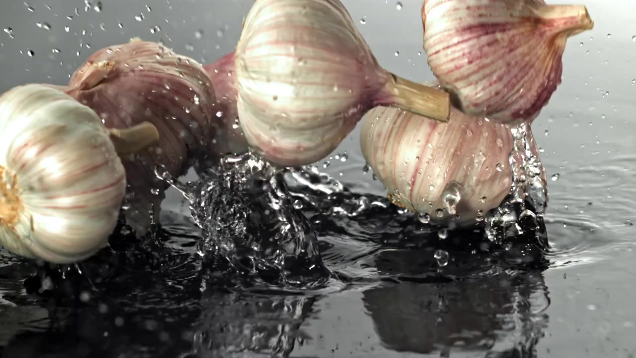 Bulbi d'aglio freschi che cadono nell'acqua al rallentatore