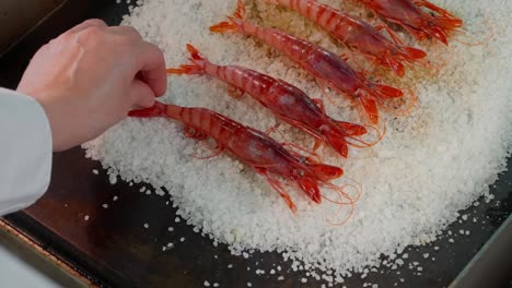 hand serves red shrimp on a plate on a wooden table