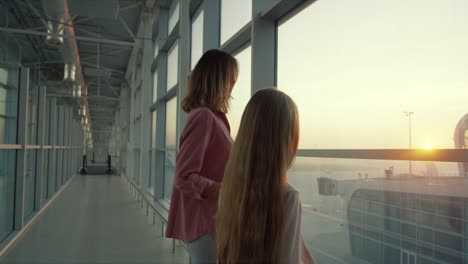 Back-View-On-The-Beautiful-Mother-And-Her-Teen-Little-Daughter-Standing-At-The-Airport-Window-And-Looking-Outside