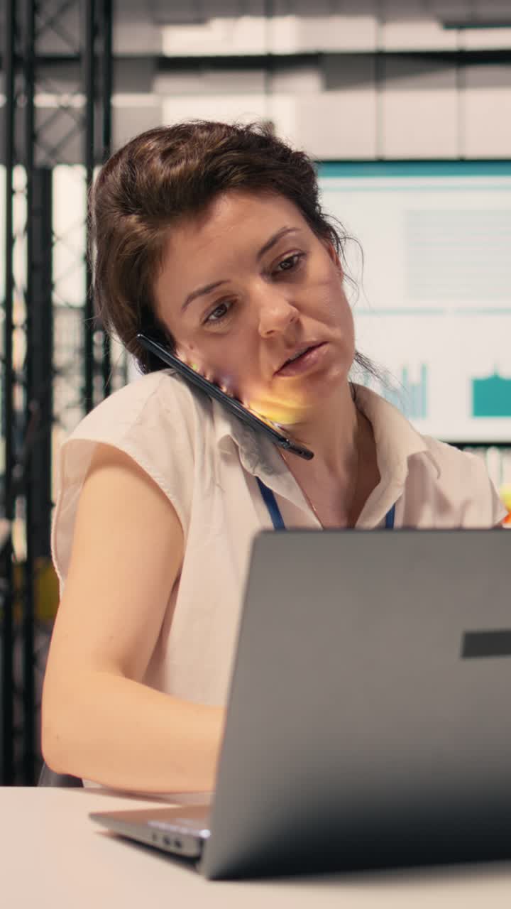 Video verticale. Donna d'affari che effettua una telefonata in un ufficio moderno, analizzando dati visivi.