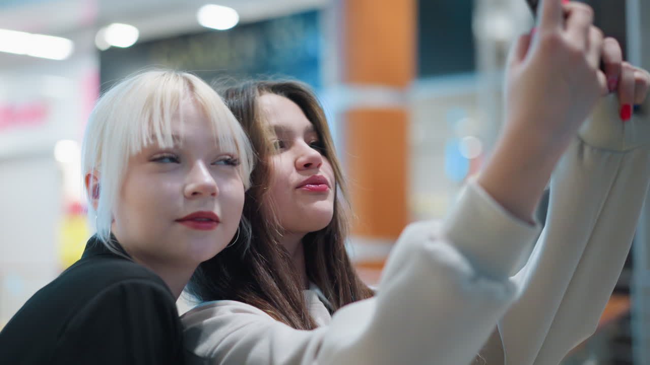 Two girls pose closely while taking selfie with smartphone indoors showing playful expressions stylish fashion and youthful energy creating modern lifestyle moment full of connection