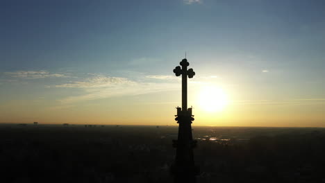 an aerial shot of a cathedral's steeple with a cross on top, taken at sunrise