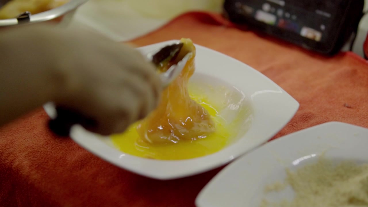 Close view of hand whisking egg mixture in bowl, liquid being blended for coating chicken, preparation step before breading, simple homemade cooking process in kitchen