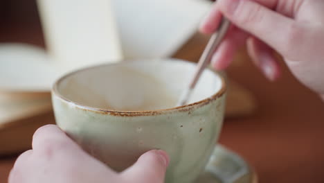 close up view of hand gently stirring coffee in ceramic cup on wooden table with soft lighting, evoking warm cozy indoor atmosphere perfect for relaxing break or morning routine moment