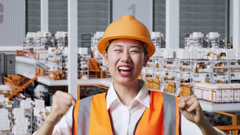 primer plano de ingeniera asiática con casco de seguridad gritando gol y bailando celebrando mientras estaba de pie en el almacén con estantes llenos de mercancías de entrega