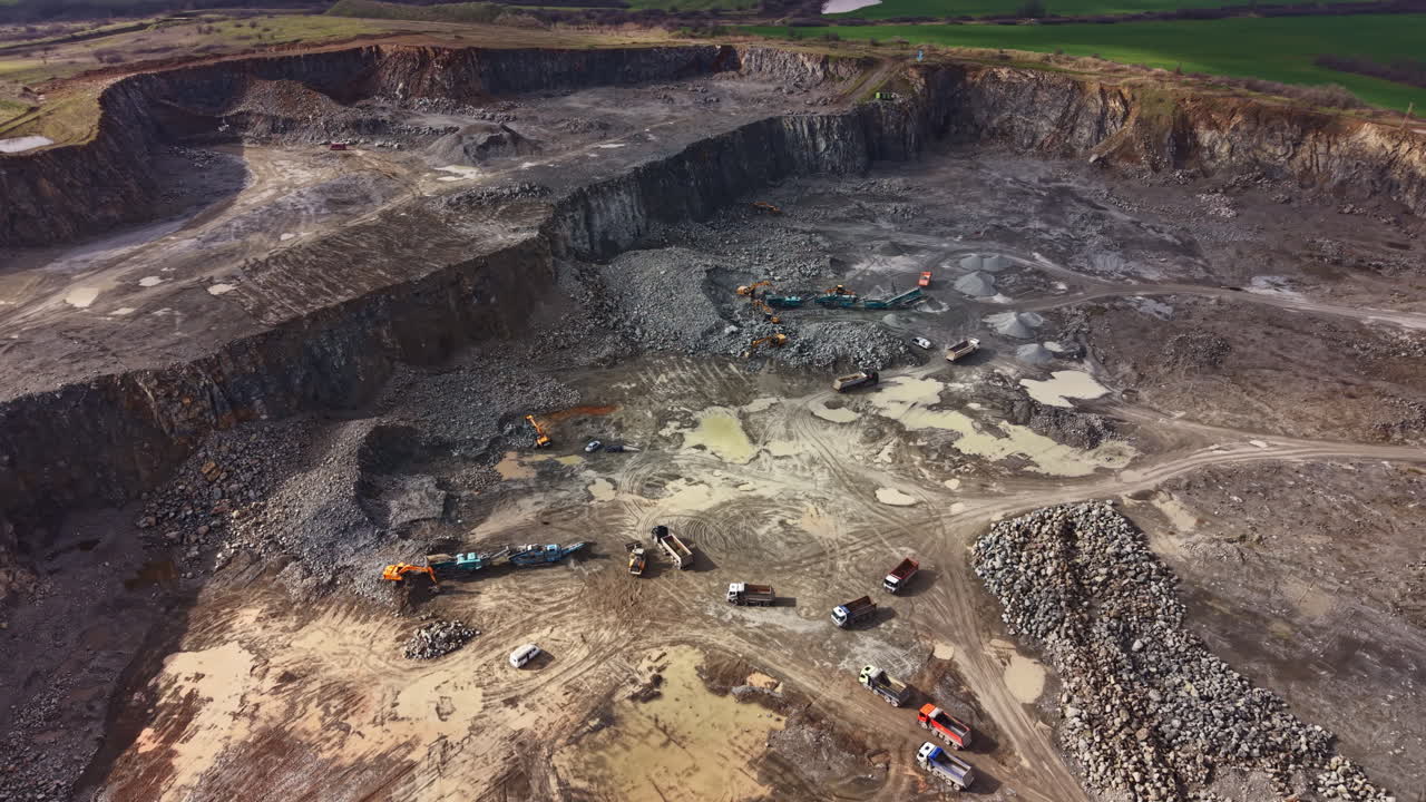 Granite quarry in operation with heavy machinery moving and large rock piles during daylight hours in a rural setting