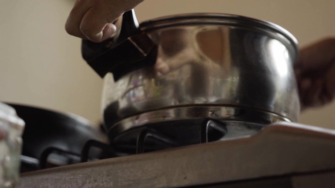 Closeup view of person placing metal cooking pot on kitchen gas stove during meal preparation inside home kitchen