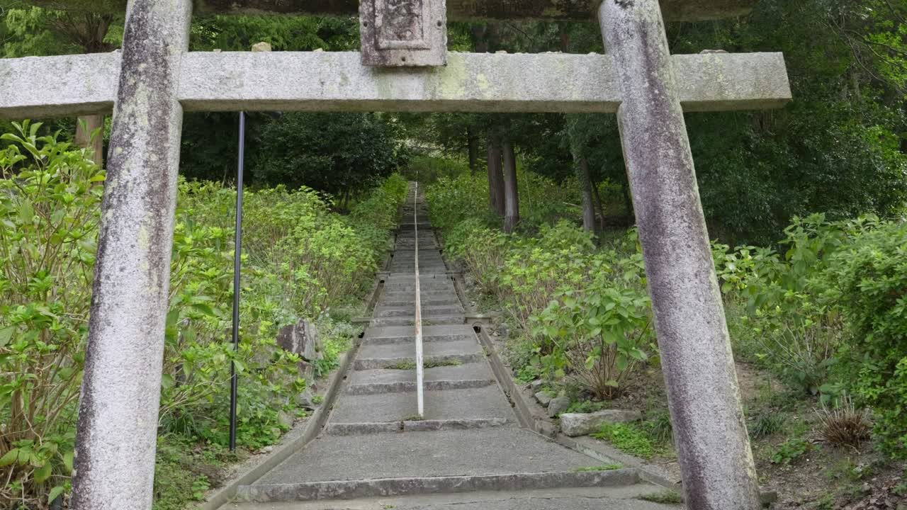 Slow motion push in toward stone torii gate at Japanese shrine