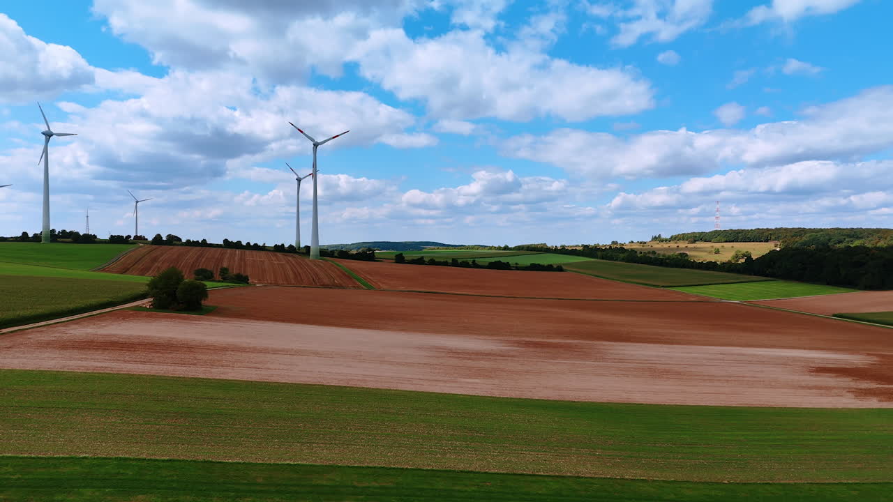 Going up over the green field. View on the wind farms rotating in the wind at backdrop. Green energy concept