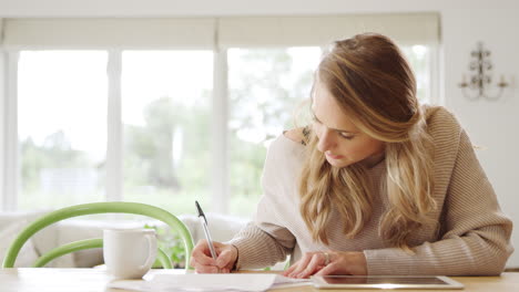 woman with digital tablet sitting at table at home reviewing domestic finances