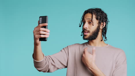 happy man chatting with friend in smartphone online videocall, studio background
