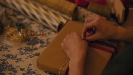 woman tying ribbon on gift box at table