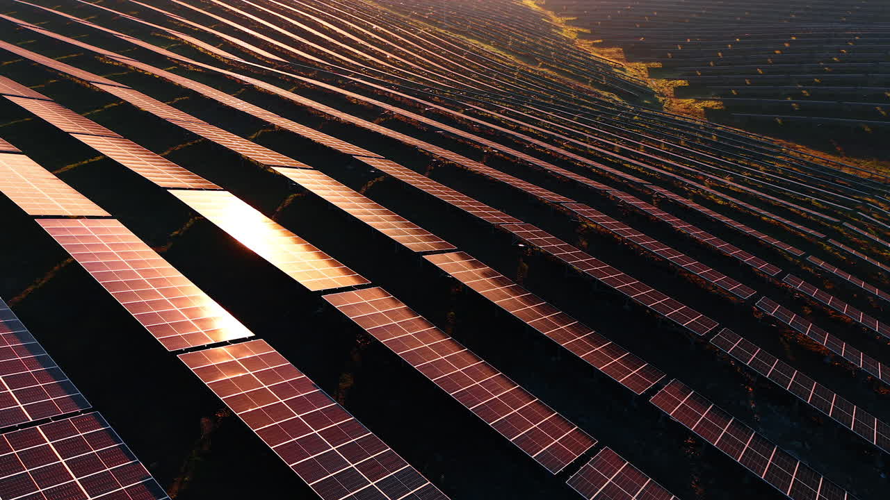Solpaneler dækker jorden over et stort område, mens solen går ned. Scenen viser rækker af paneler, der reflekterer lys og producerer energi på et anlæg for ren energi