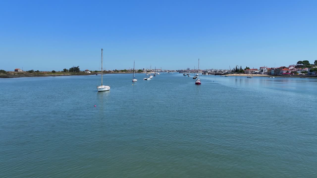 Drone shot flying low over water among anchored sail yachts