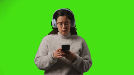 Mujer-Joven-Con-Auriculares-Inalámbricos-Transmitiendo-Música-Desde-Un-Teléfono-Móvil-Contra-La-Pantalla-Verde-Del-Estudio-2