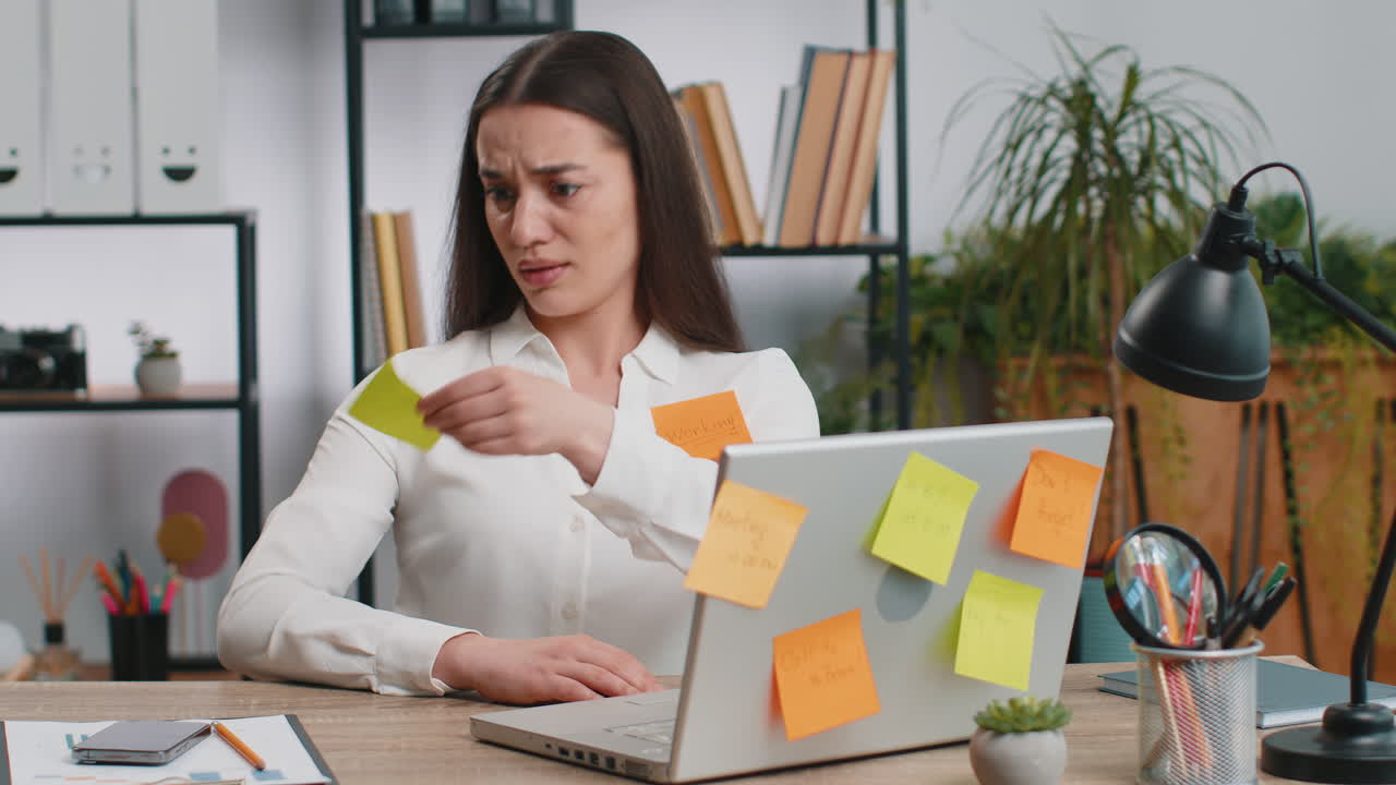 Tired sad exhausted businesswoman working on laptop at office with many sticker tasks panic attack