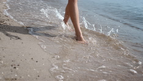 las piernas de una mujer en primer plano caminando en la arena húmeda cerca de las olas del océano. una chica saltando sobre el agua del mar.